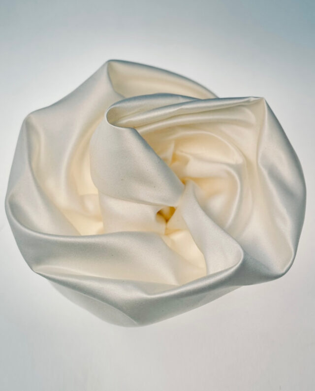 Satin Rosette – Ivory A soft, sculptural satin rosette in timeless ivory. Each piece is handmade and finished with a brooch pin on the back, making it easy to attach to dresses, blazers, or belts for a refined and eye-catching touch.