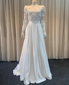 A refined two-piece set featuring a delicate lace top with long sleeves, paired with a flowing duchess satin skirt. Designed by Rikke Gudnitz.