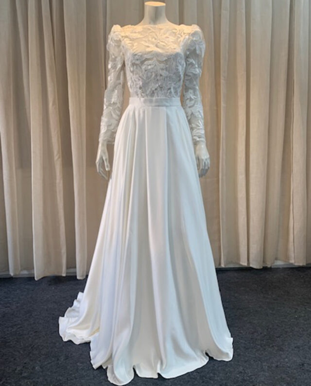 A refined two-piece set featuring a delicate lace top with long sleeves, paired with a flowing duchess satin skirt. Designed by Rikke Gudnitz.